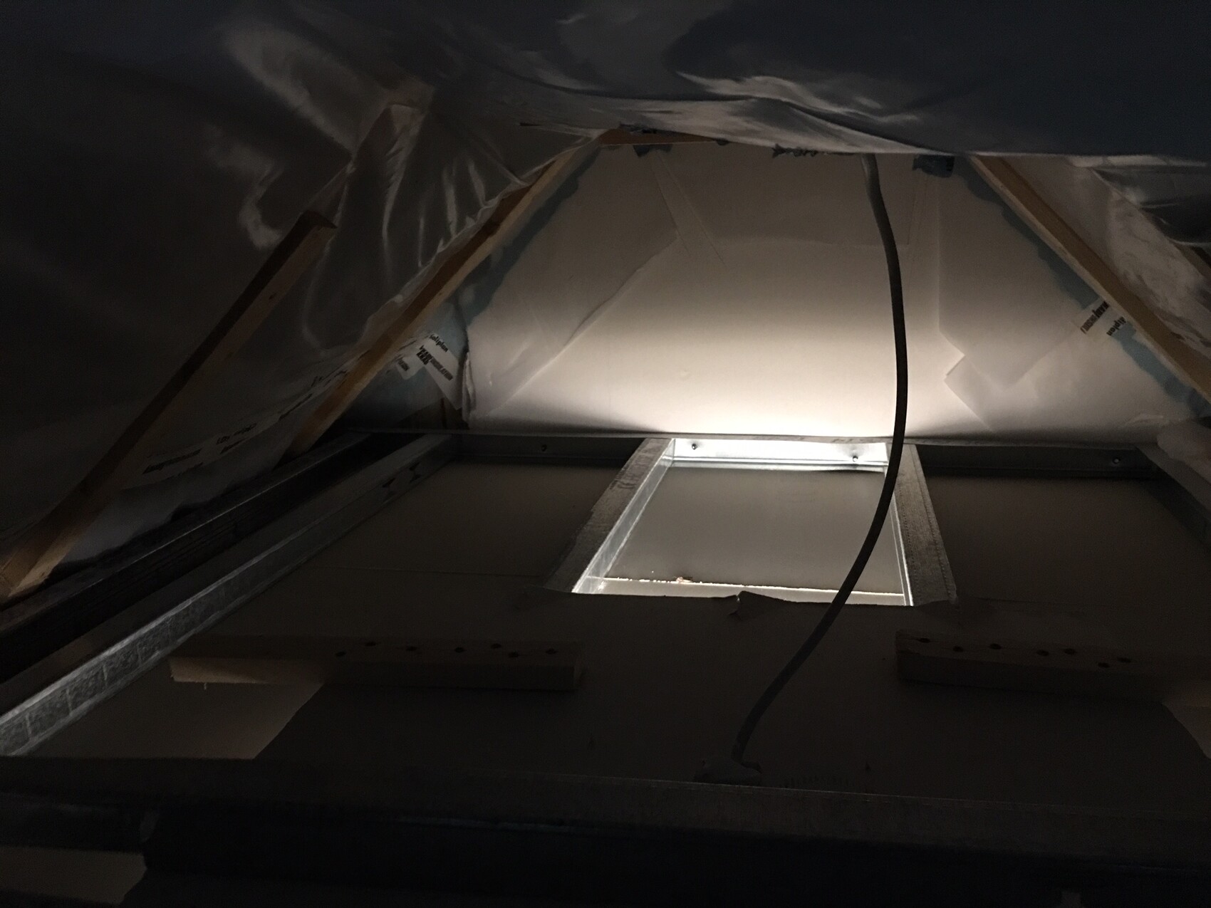 Interior photo of an attic with insulation, membrane, wooden frame, and cables