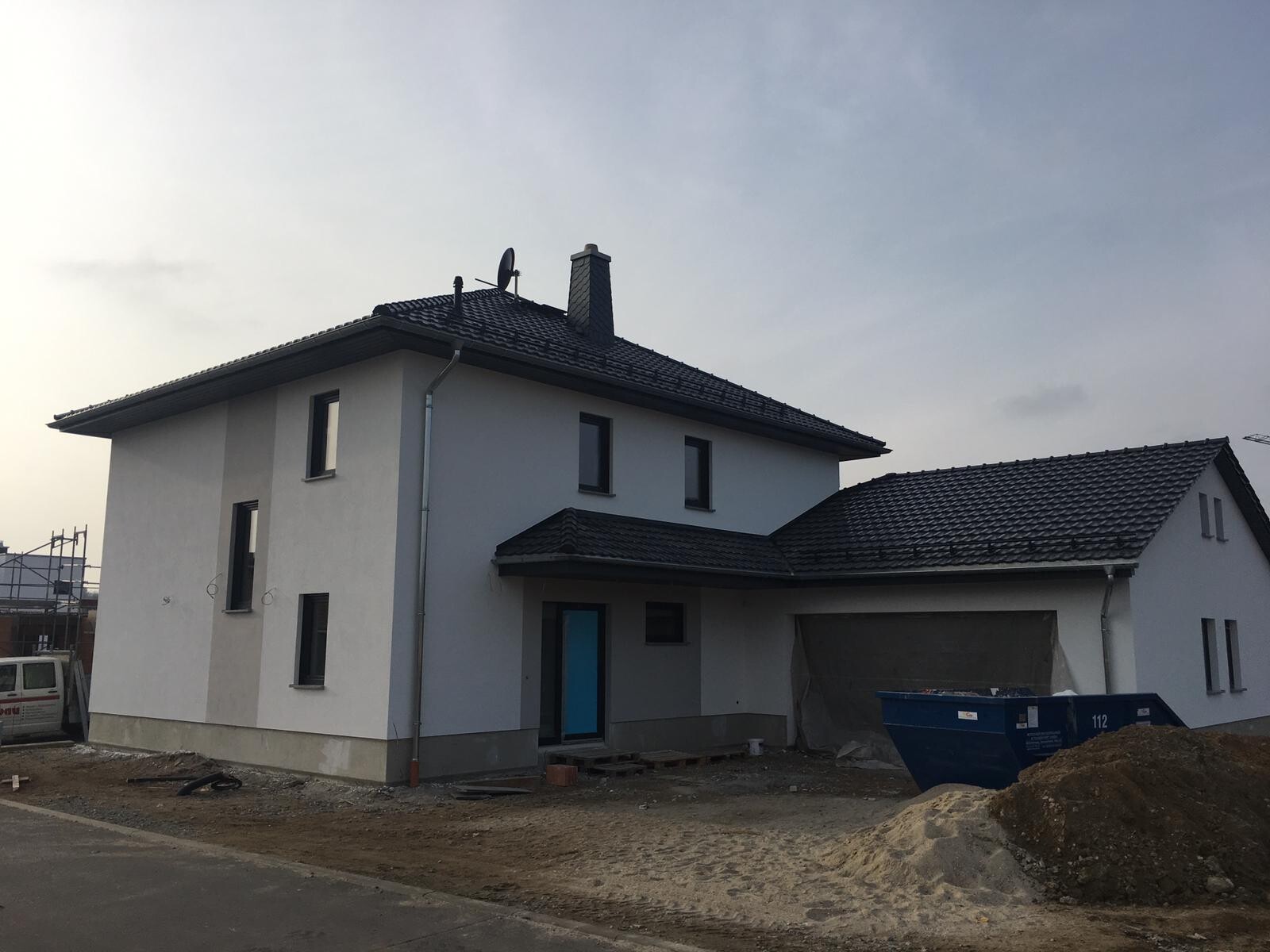 New build house at shell stage with roofing work, construction site and site container.