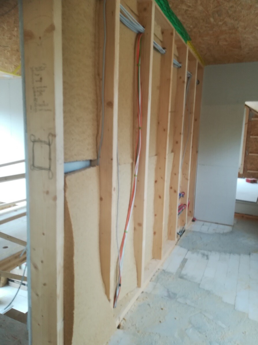 Unfinished interior wall with wooden studs, insulation, and visible cables at a construction site.