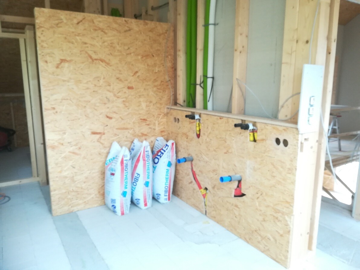 Interior view of a construction site: OSB wall, pipes, and insulation bags.