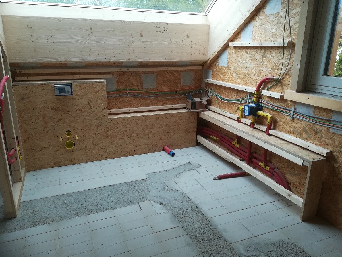 Interior of a construction site with OSB walls, skylight, red piping system, cables, and workbenches.