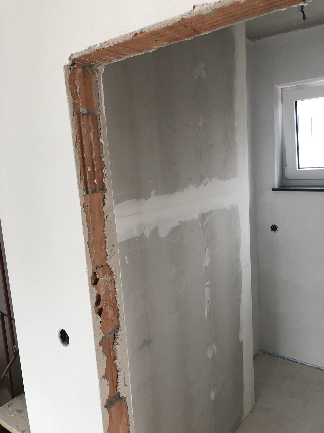 Indoor construction site: exposed brick wall at door frame, plastered interior wall and window to the right.