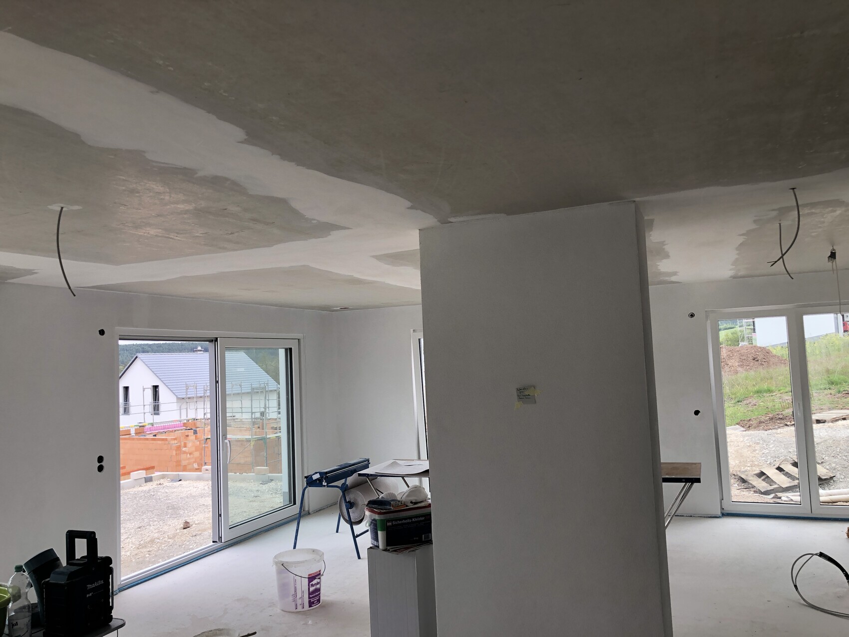 Unfinished interior: ceiling filling work, central column, construction tools, glass sliding doors