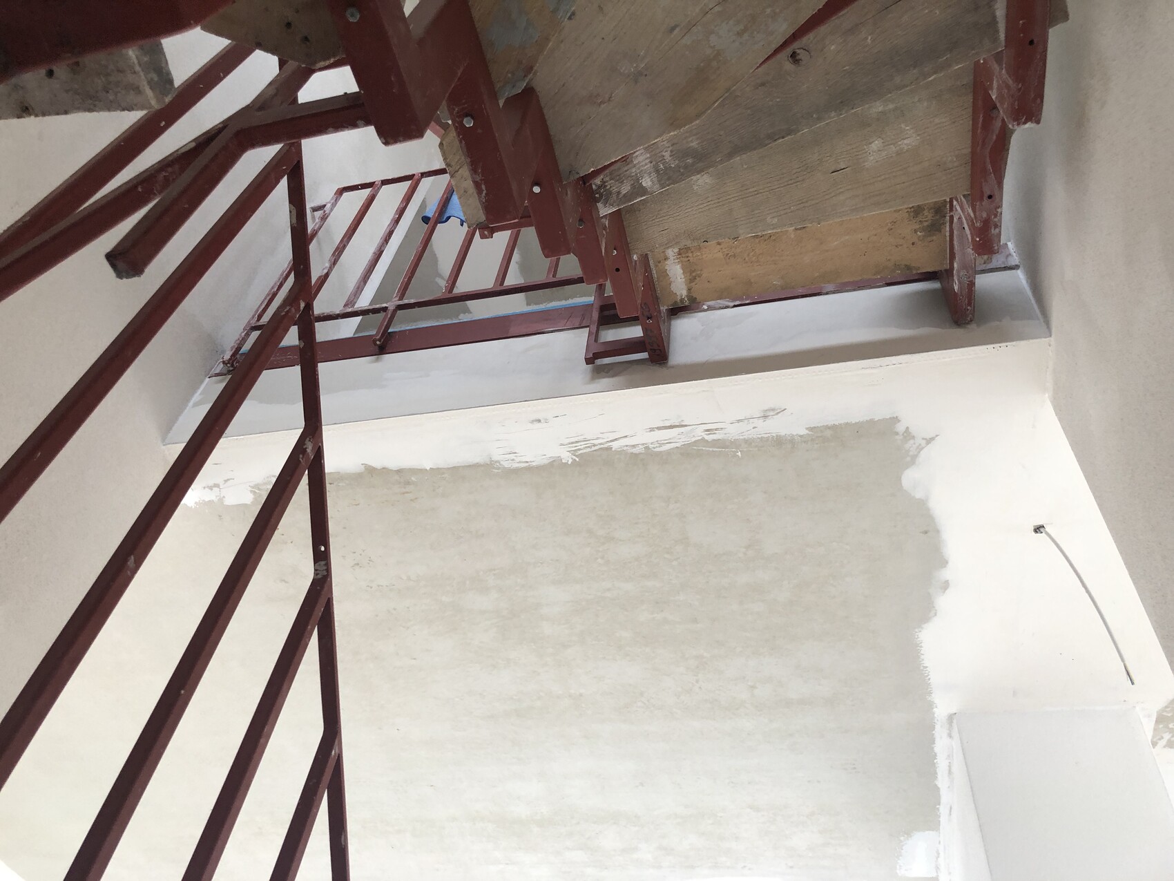 Interior view of staircase construction area: red railing, wooden floorboards, unplastered walls.