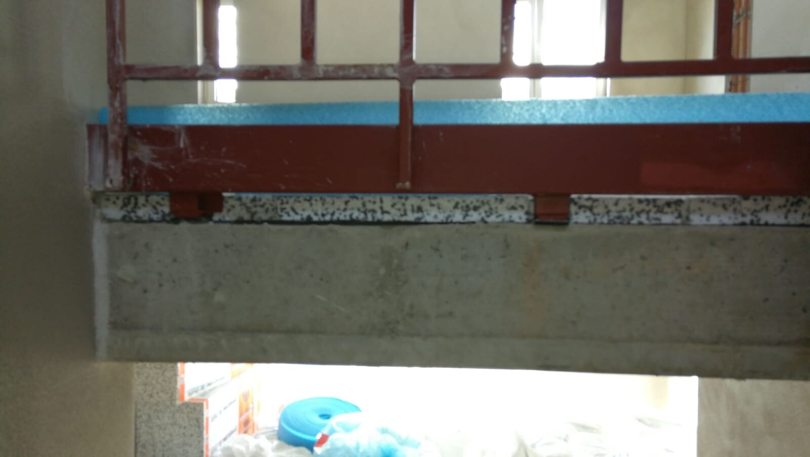 Red metal railing over a blue edge on a concrete bridge, view out into bright light.