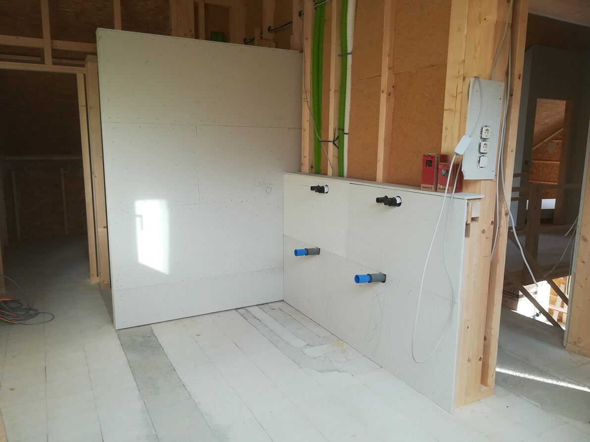 Interior of a construction site: white cabinets, blue pipe connections and timber frame construction.