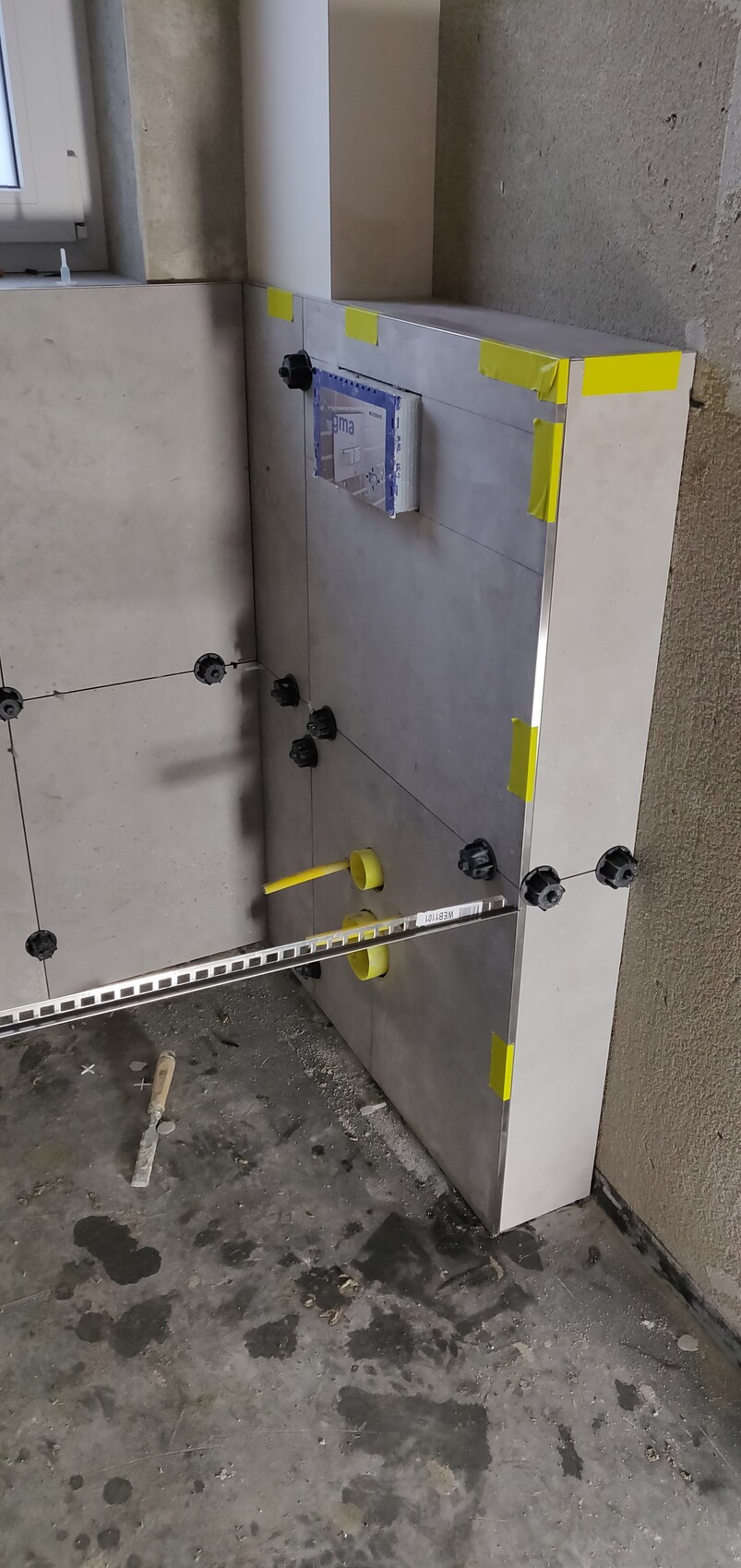 Bathroom construction site: tiling work, yellow mounting discs, wedges, and metal rail installed.