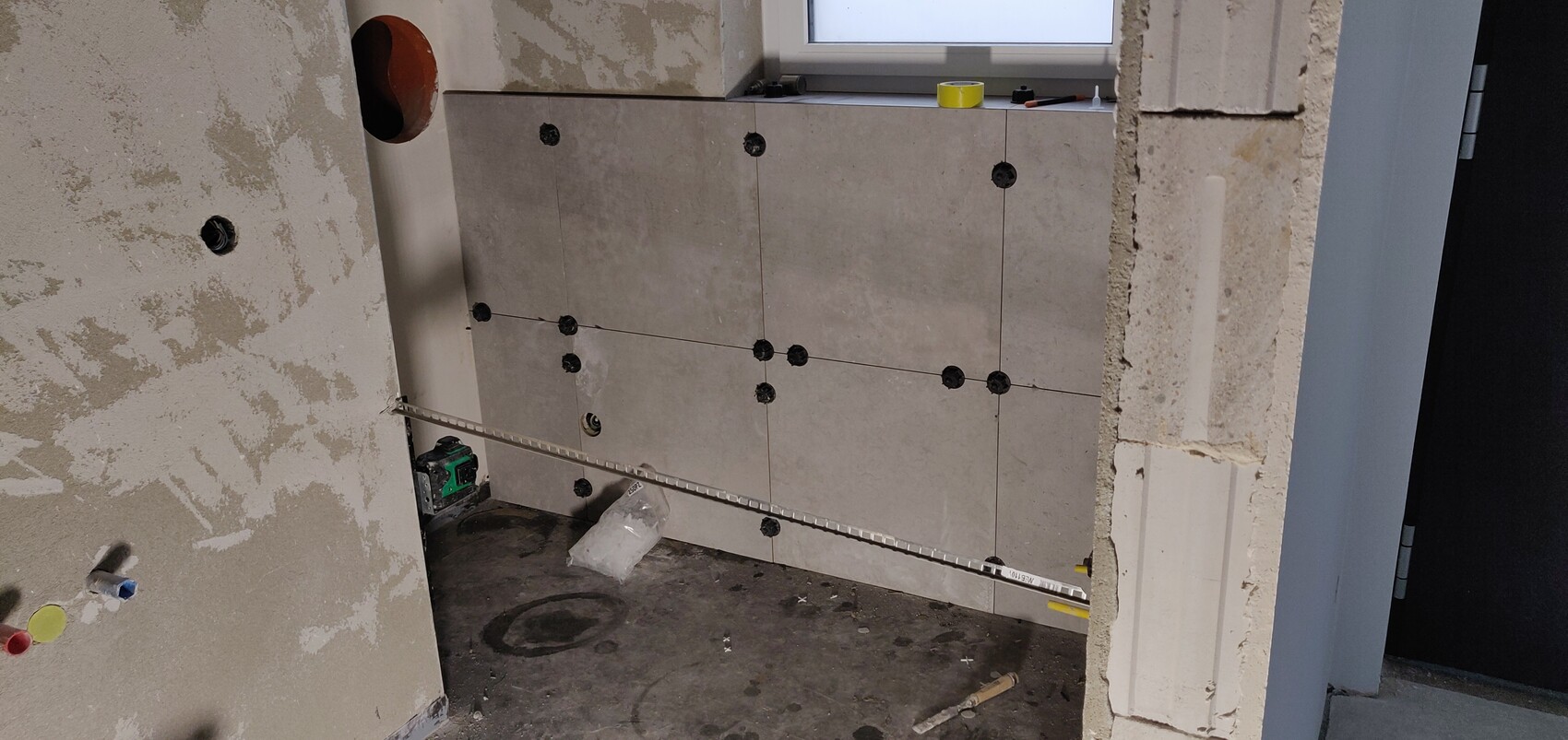 Bathroom construction with wall tiles, visible tile spacers, spirit level, and tools on the floor.