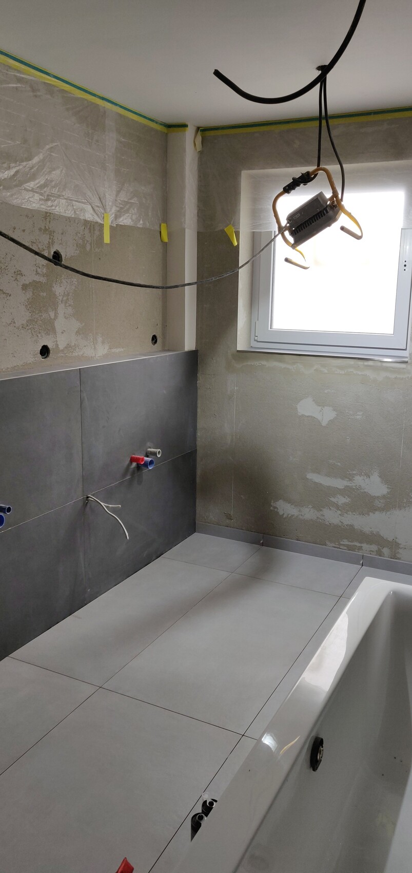 Bathroom under renovation: exposed water pipes, cables, unfinished walls, and bathtub.