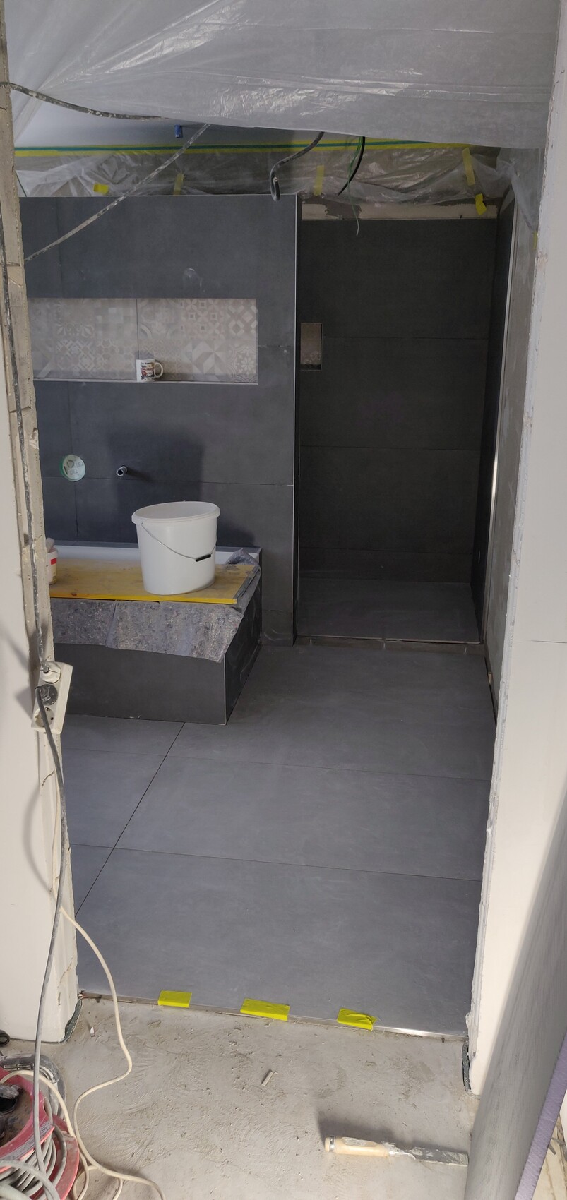Bathroom renovation: dark tiles, bucket on stone platform, plastic sheeting on ceiling.