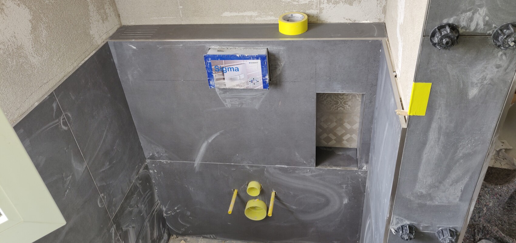 Bathroom area with dark tiles, open cutout, yellow piping and Sigma packaging