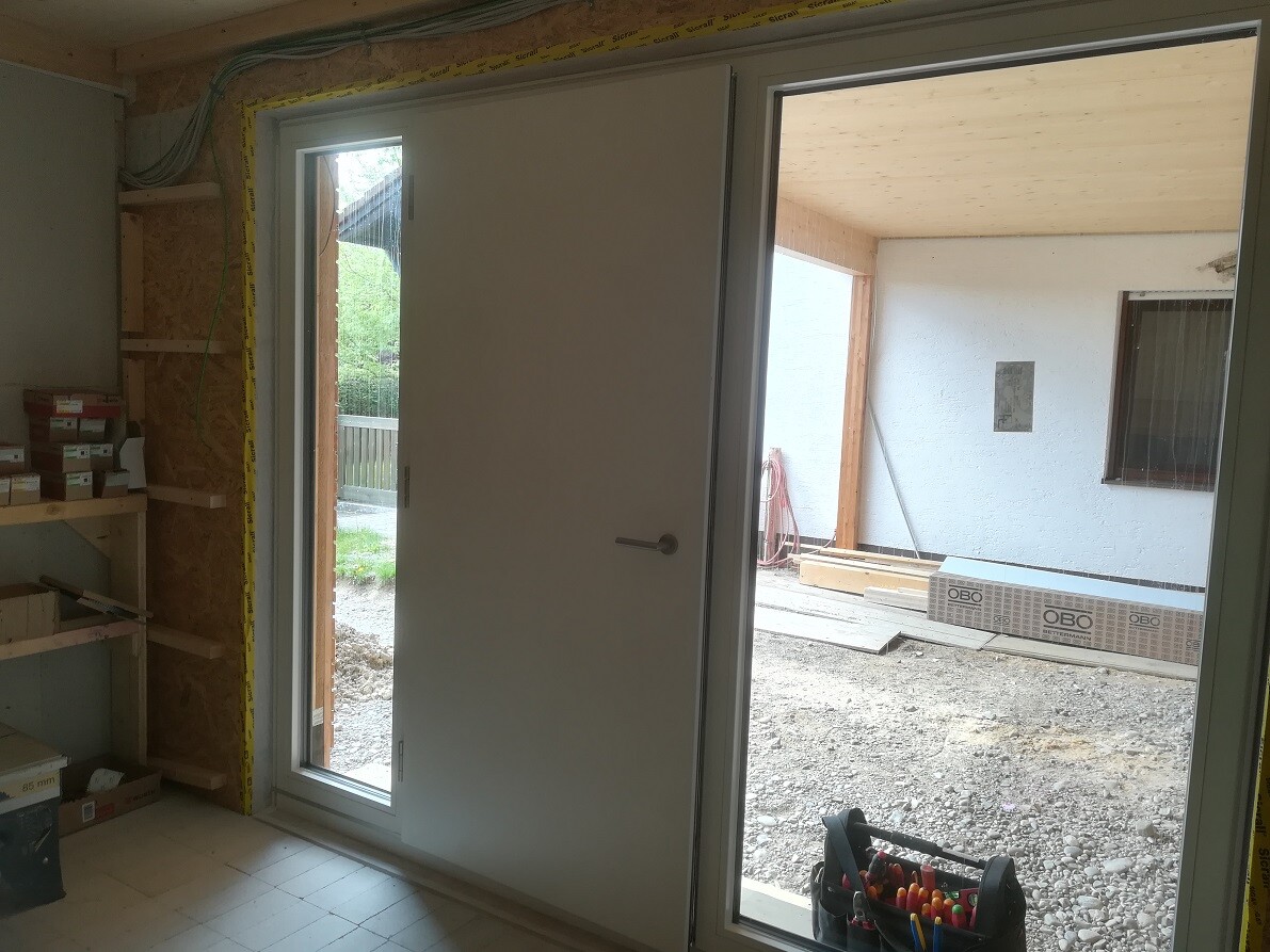 Interior of a construction site: door opening outward, window on the right, construction timber, tool basket in front.