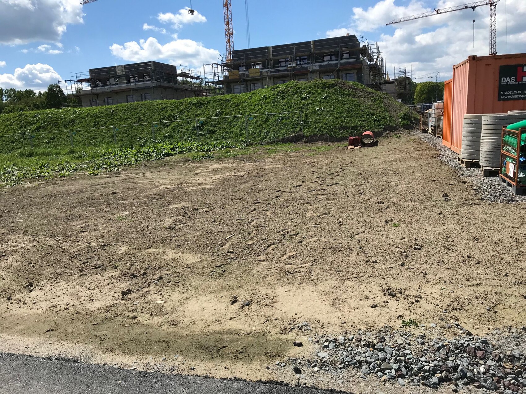 Construction site with unpaved ground, scaffolding, cranes, construction containers, and building materials.