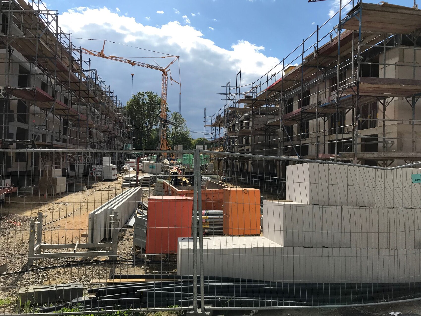 Construction site: scaffolding on two buildings, crane in the background, building materials and fence.