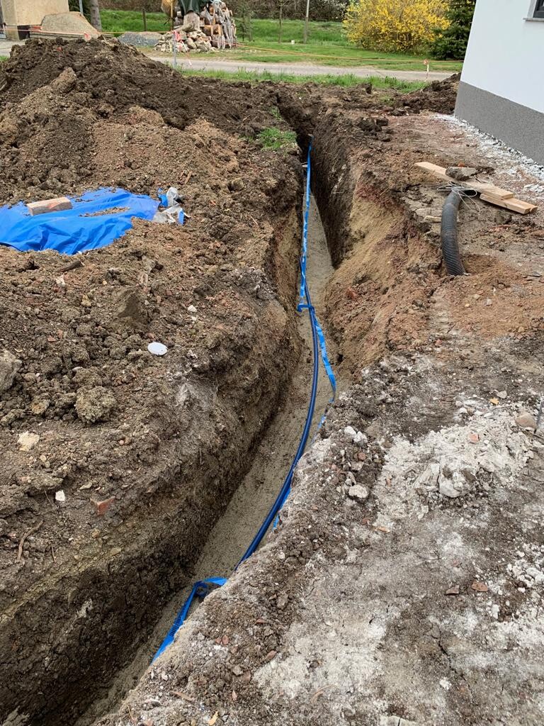 Construction pit next to the house with laid blue pipe/line in the ground and loose soil.