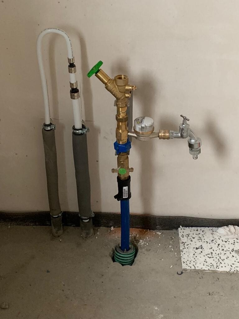 Water installation setup with meter, valve, fittings, and pipes on the wall.