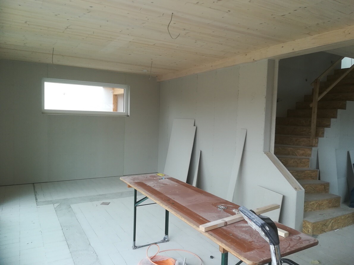 Room in shell construction with wooden ceiling, small window, stairs and workbench with building materials.