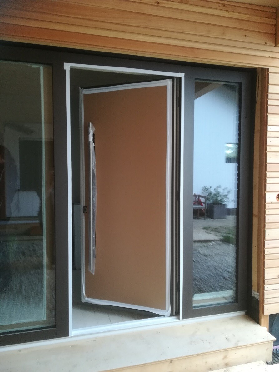 Brown front door hangs crookedly in an open frame of a wooden facade next to glass windows.