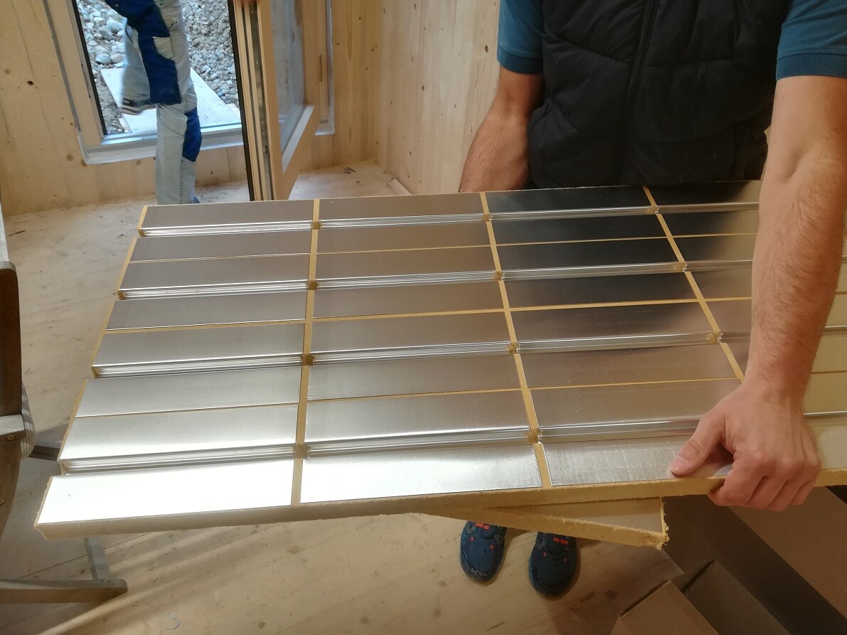 Person holding a panel made of silver metal tiles with golden joints in a workshop.