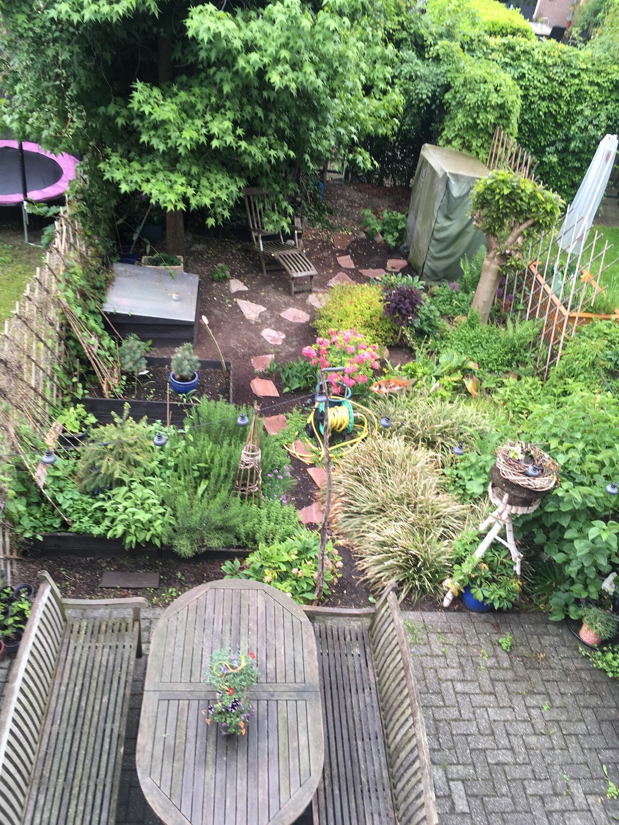 Garden in the backyard with oval wooden table and chairs, planting beds, garden path made of stone slabs.