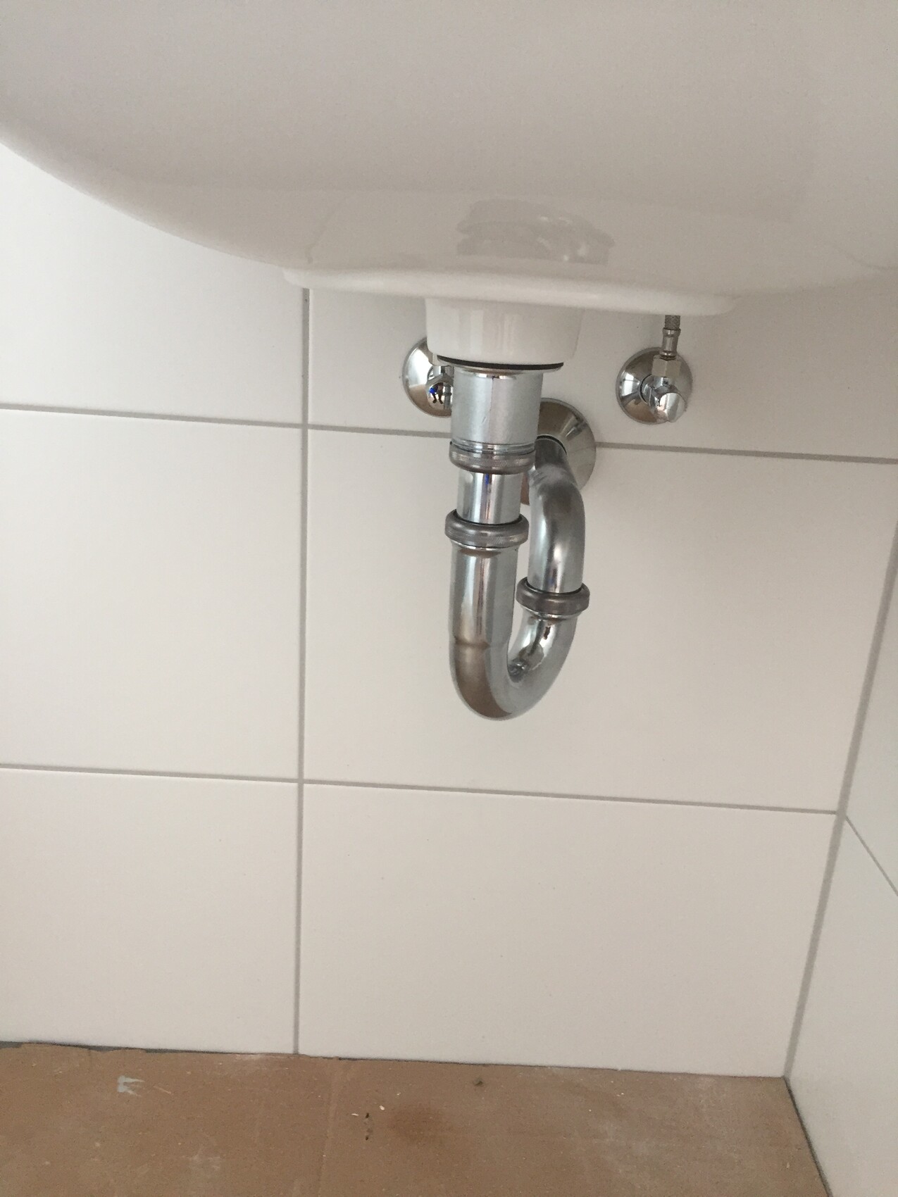 Chromed pipes and trap visible under the sink against tiled wall