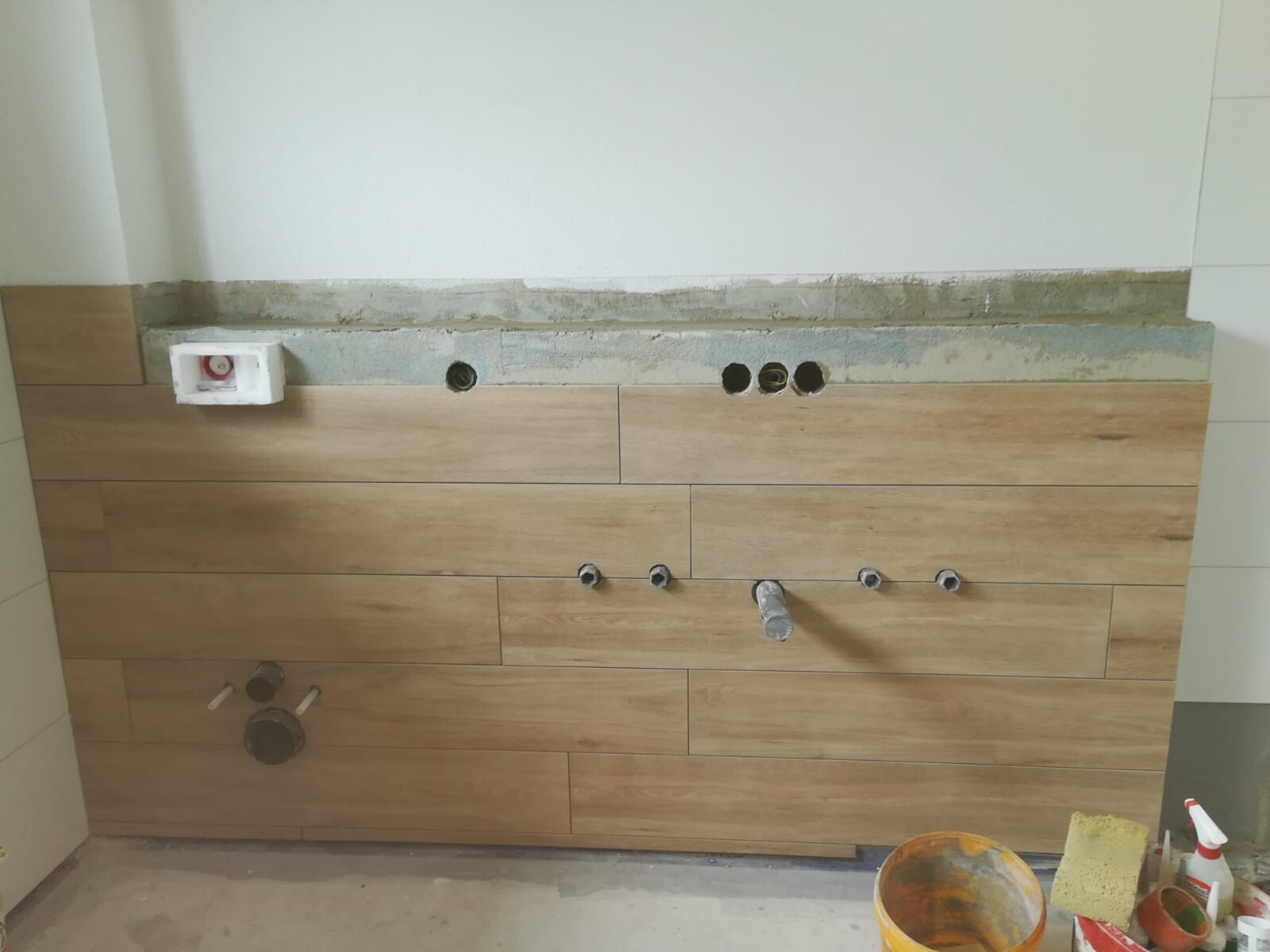 Küchenunterbau mit Holzoptik-Verkleidung, Bohrlöcher für Armaturen sichtbar, Bauwerkzeuge daneben