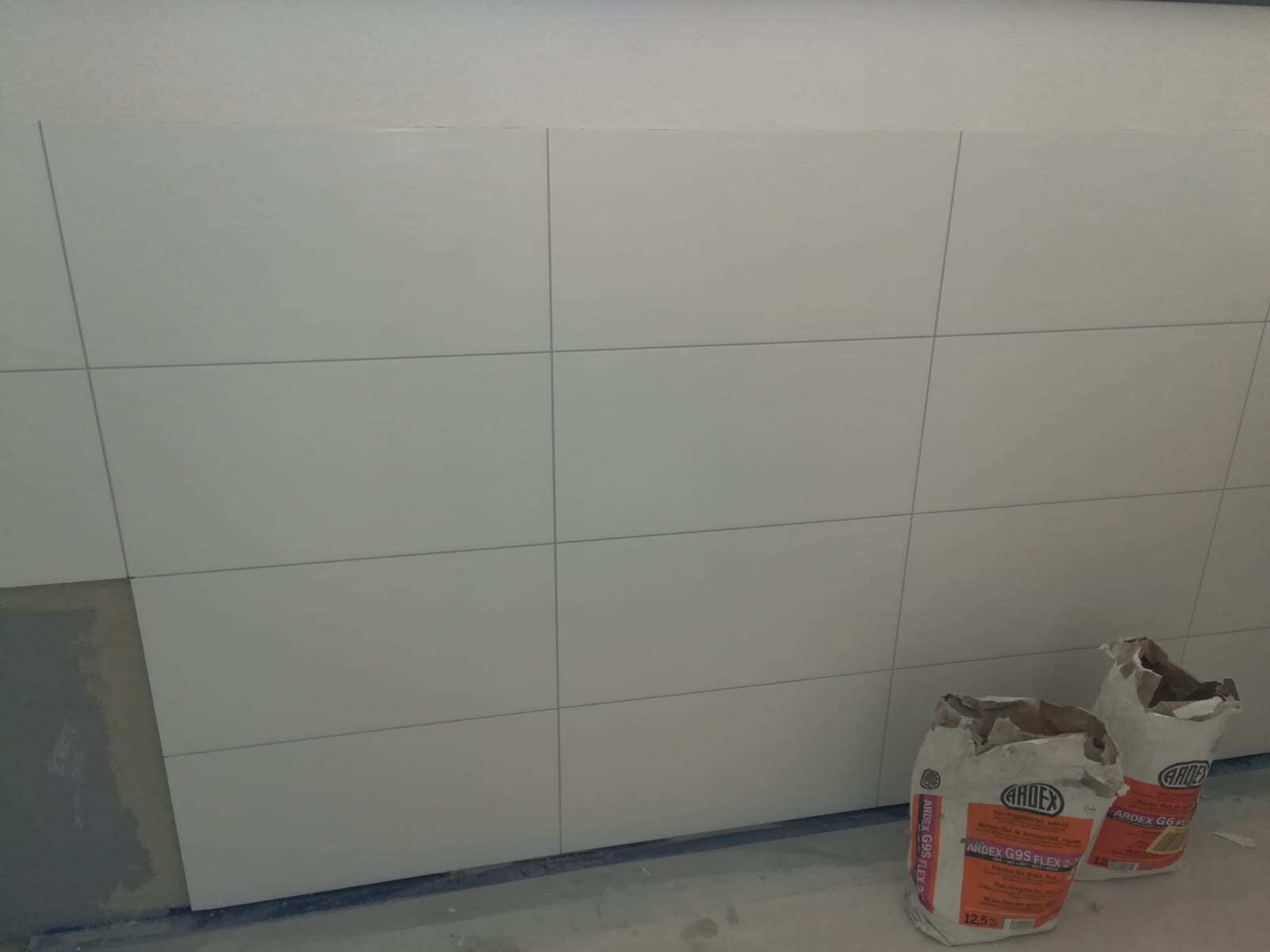 Weiße Wandfliesen auf Baustelle; zwei ARDEX-Säcke Fliesenkleber im Vordergrund.