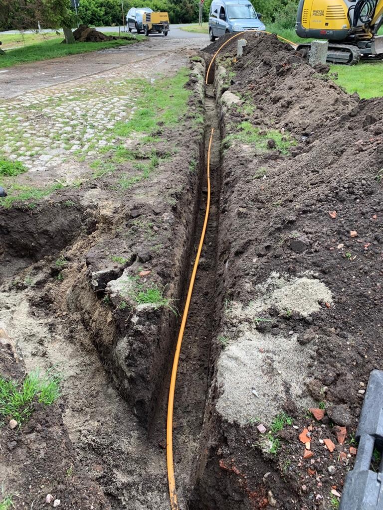 Deep trench with orange cable, construction site at roadside, excavated soil.