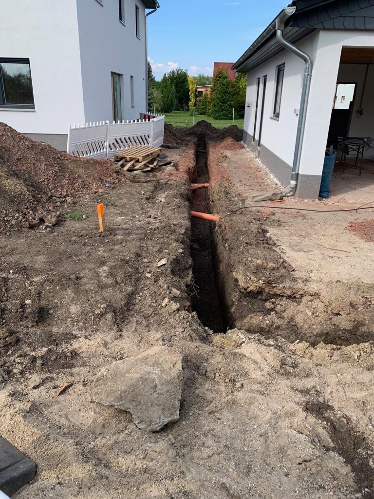 Trench between two houses during construction work, visible orange pipes.
