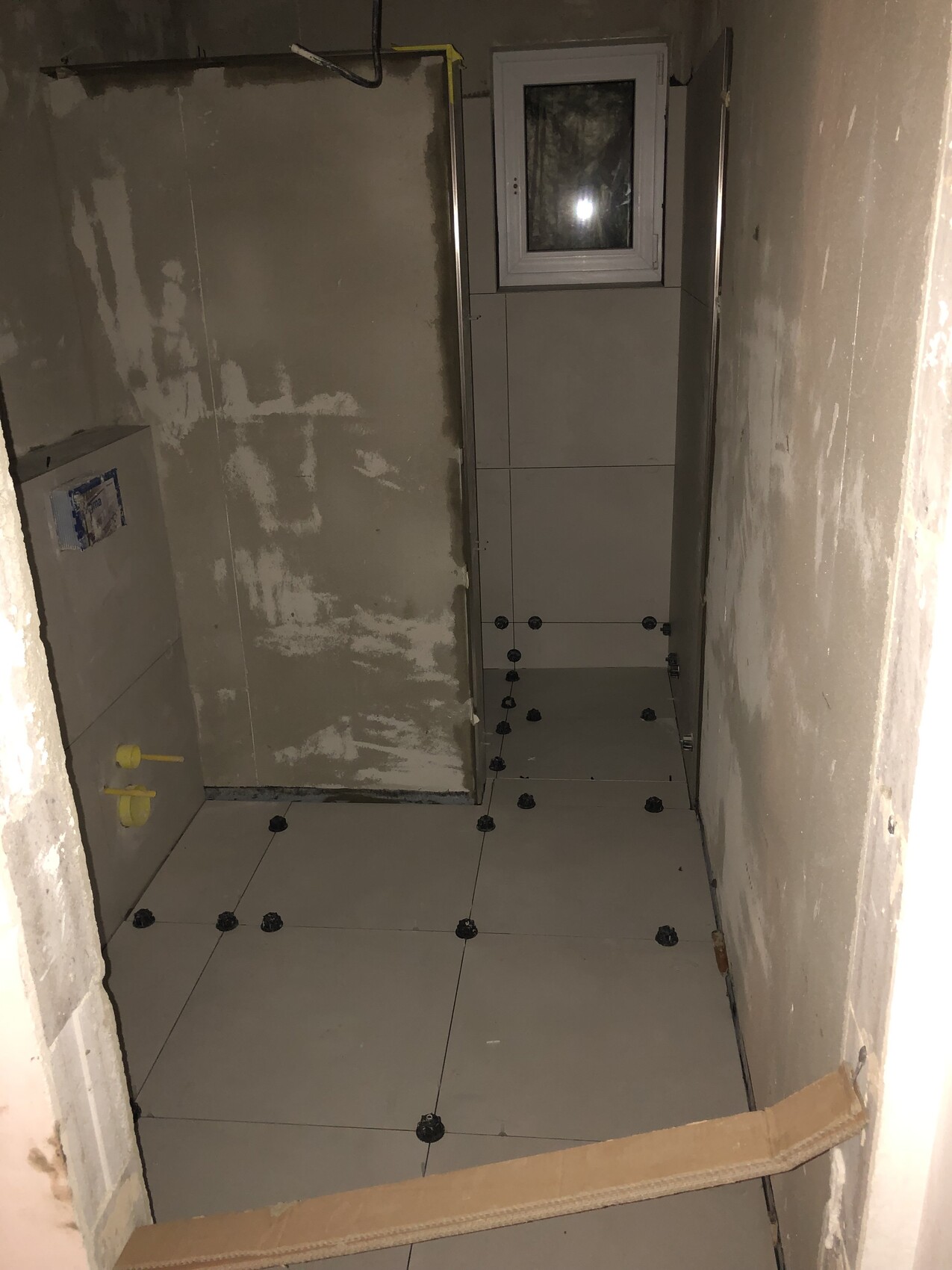 Unfinished shower room: tiles being installed, window at the back; tile spacers visible.