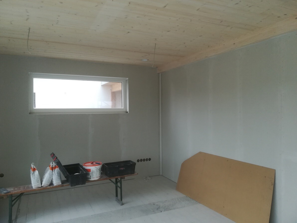 Construction room with wooden ceiling, window, workbench, construction tools, and plywood panel.