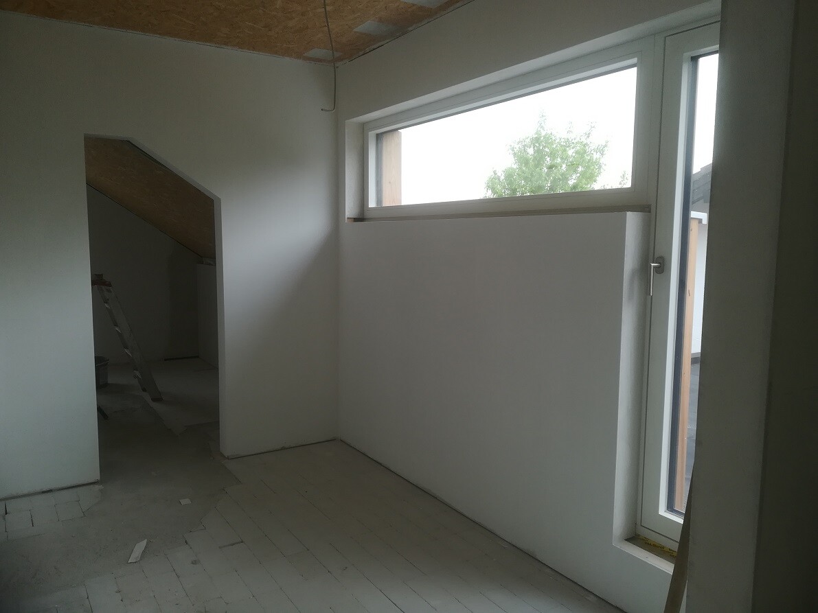 Unfinished interior in loft: white walls, ladder, tall window band, niche area.