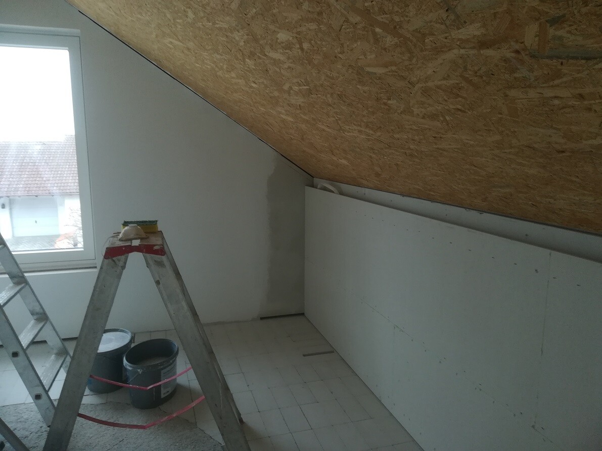 Attic renovation: ladder, paint cans, and plaster work under a sloped wooden ceiling.