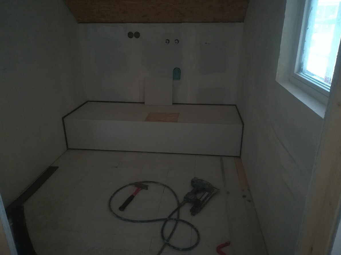Small construction site: white platform against wall, tools and cables on the floor, window on the right.