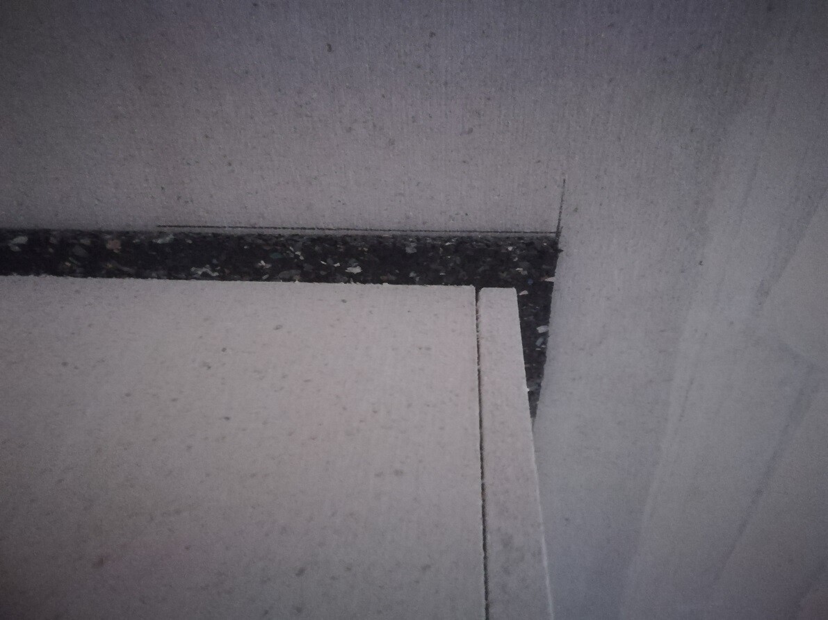 White styrofoam boards stacked in a corner in front of a gray wall; dark, grainy stripe.
