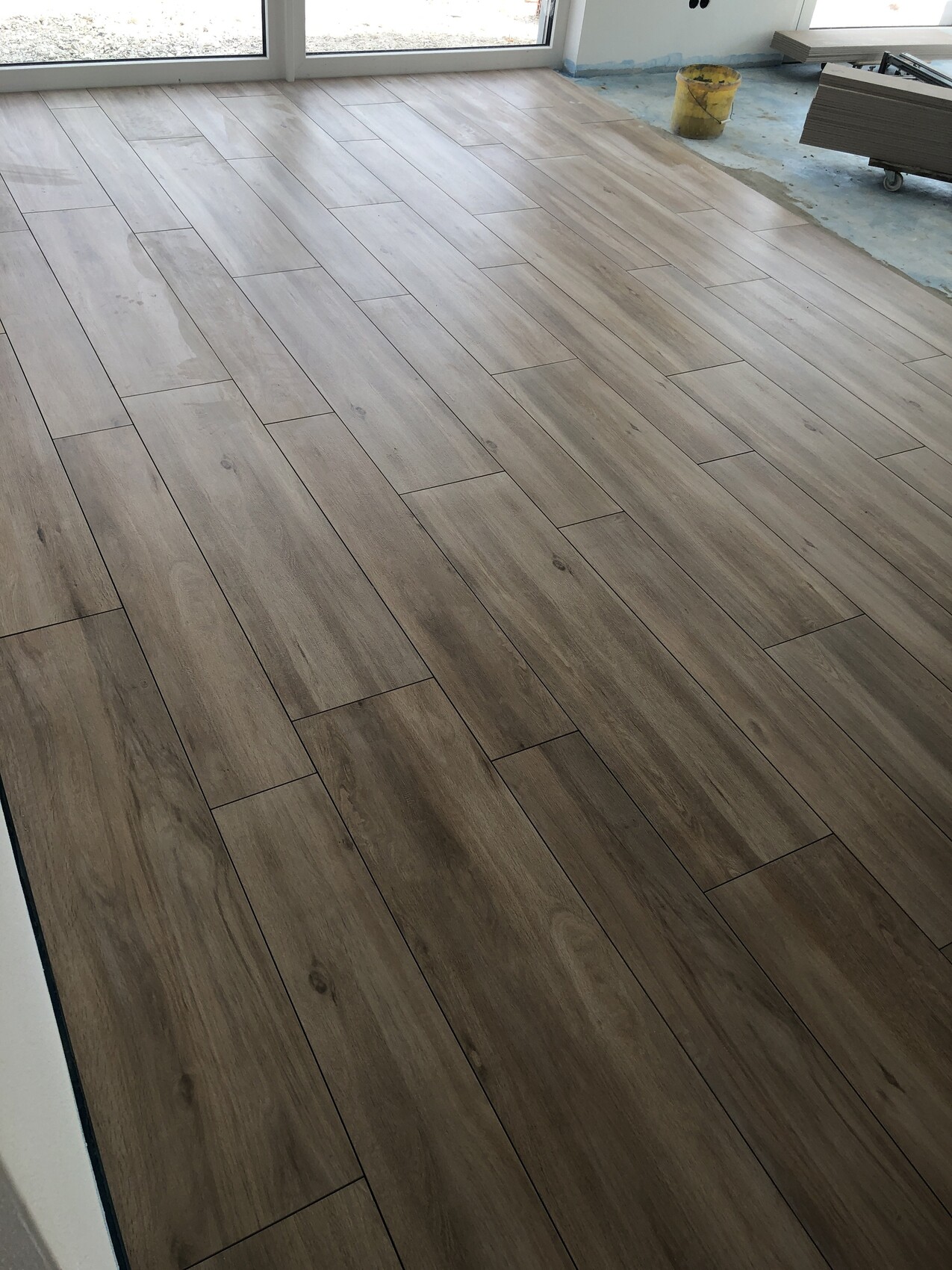 Newly installed wood-look laminate flooring in a light brown shade; construction tools along the edge.