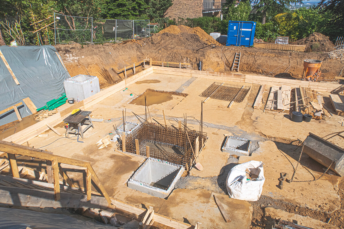 Construction site with foundation excavation, reinforcement, formwork, sand, and wooden components.
