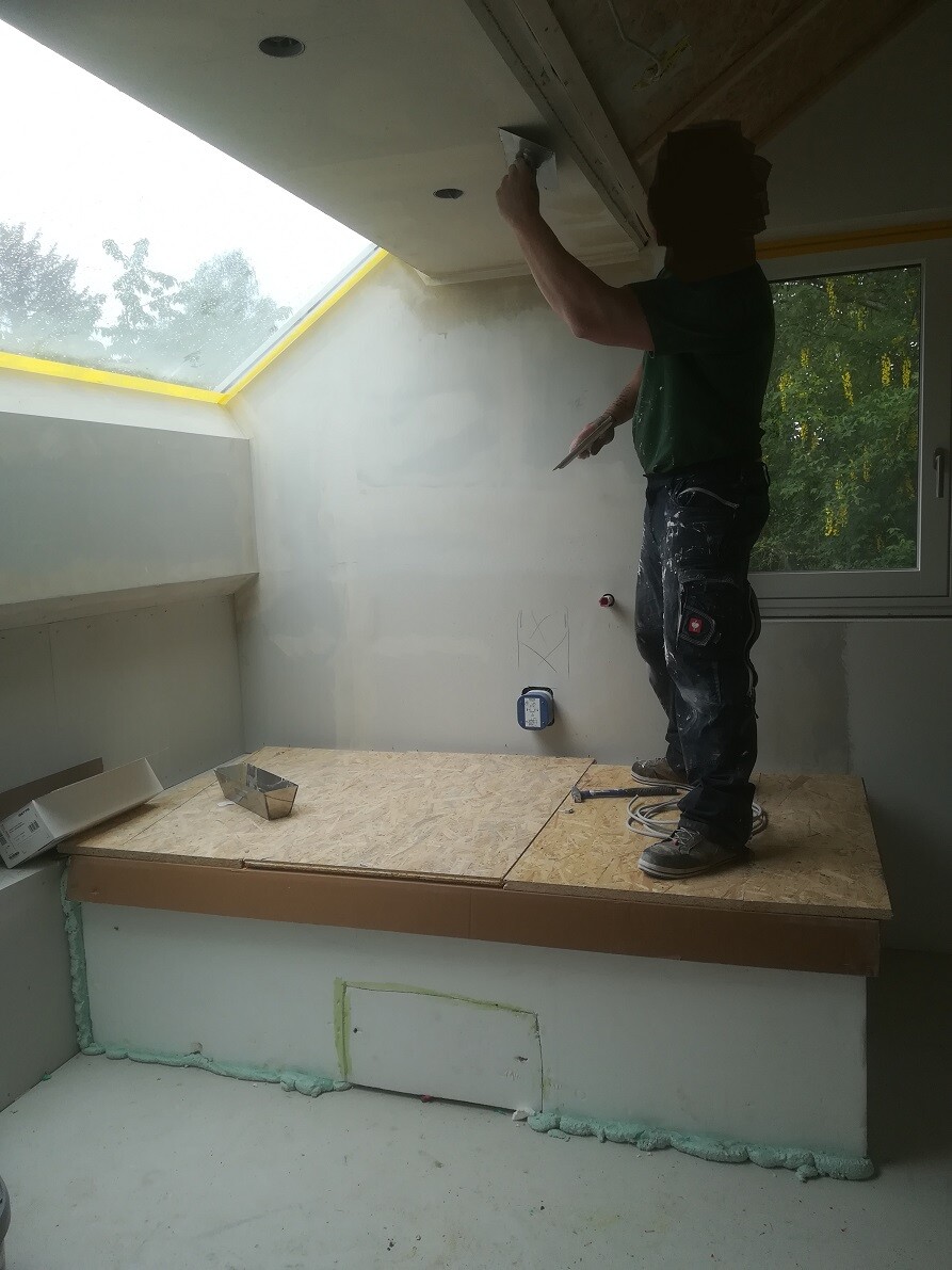 Man plastering the ceiling, standing on a wooden platform in a renovation room.