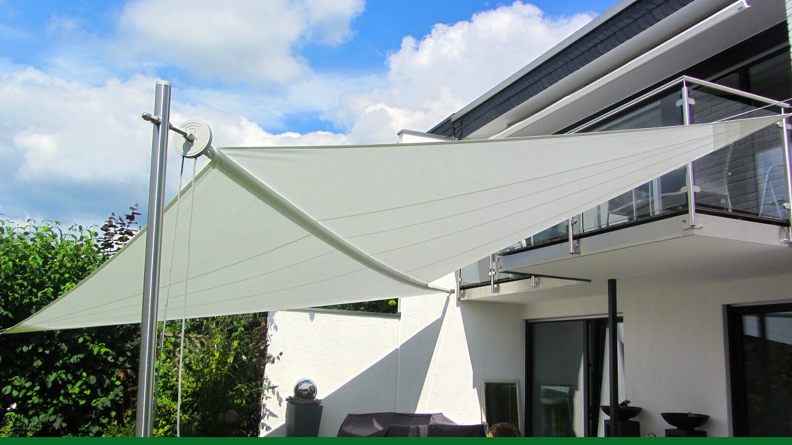 White sun sail stretched over a terrace in front of a modern house with glass railing