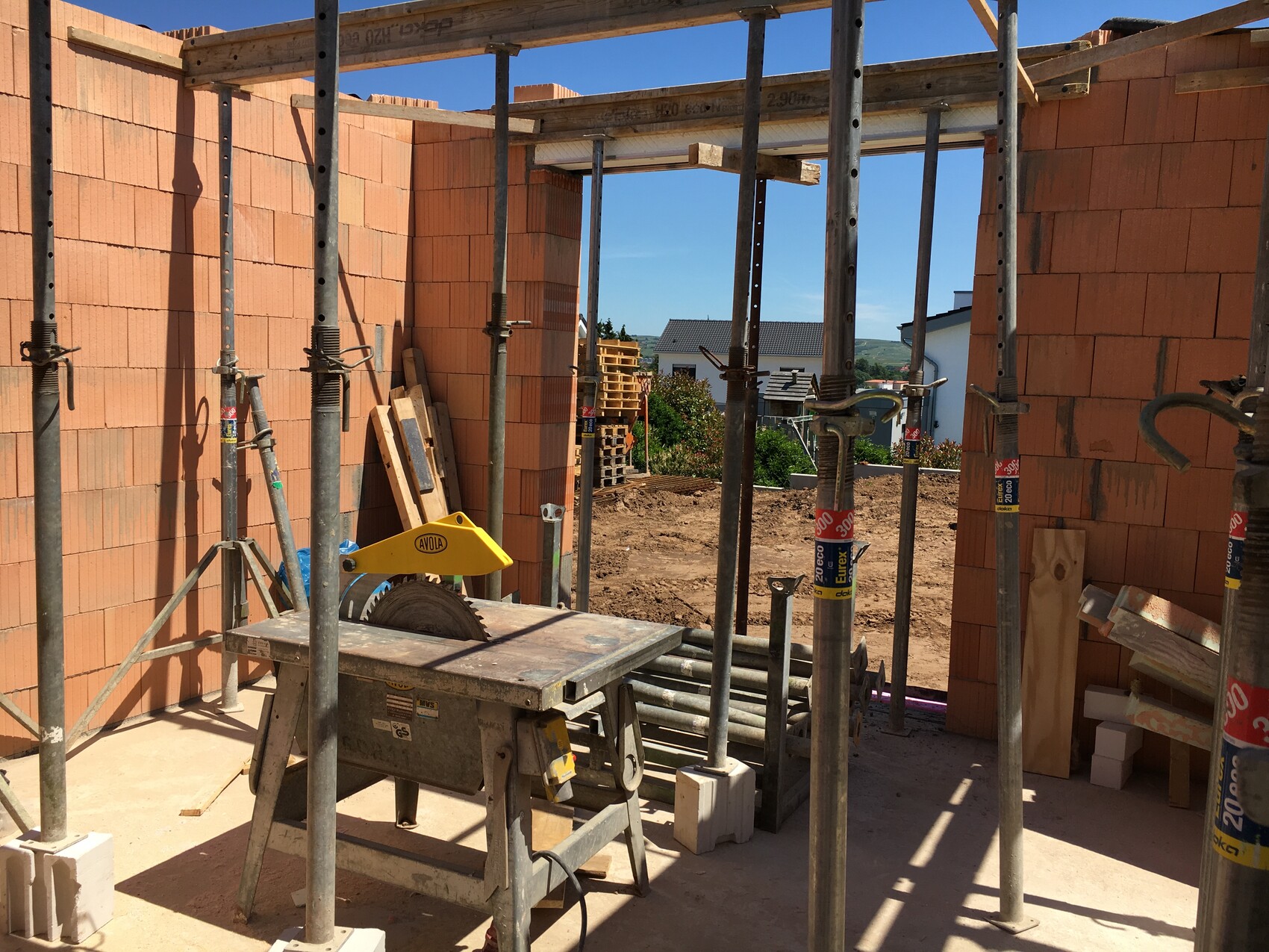 Construction site with brick walls, scaffolding poles, wooden planks, and miter saw on table.