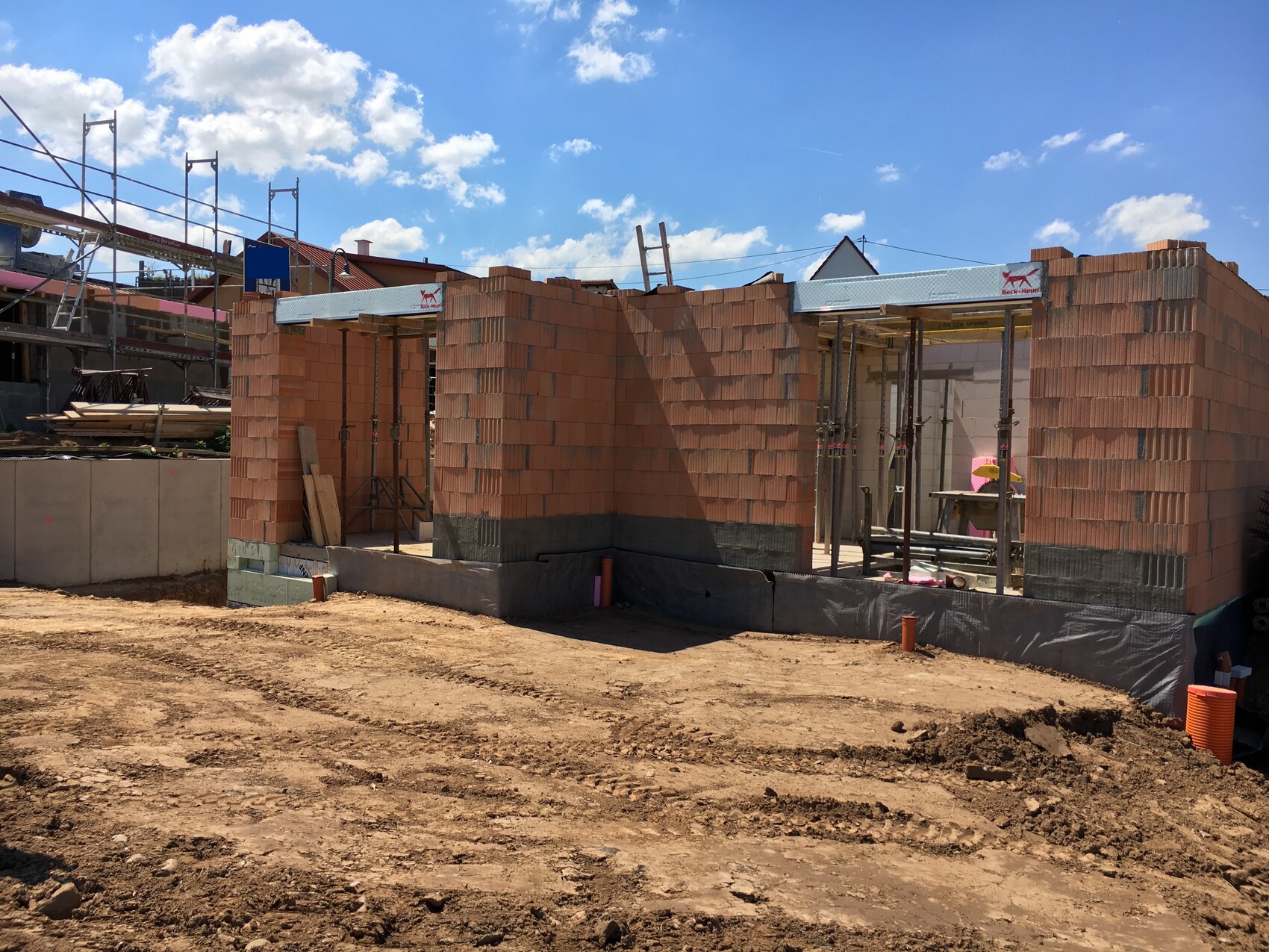 Construction site with red brick wall, scaffolding, and building materials under blue sky