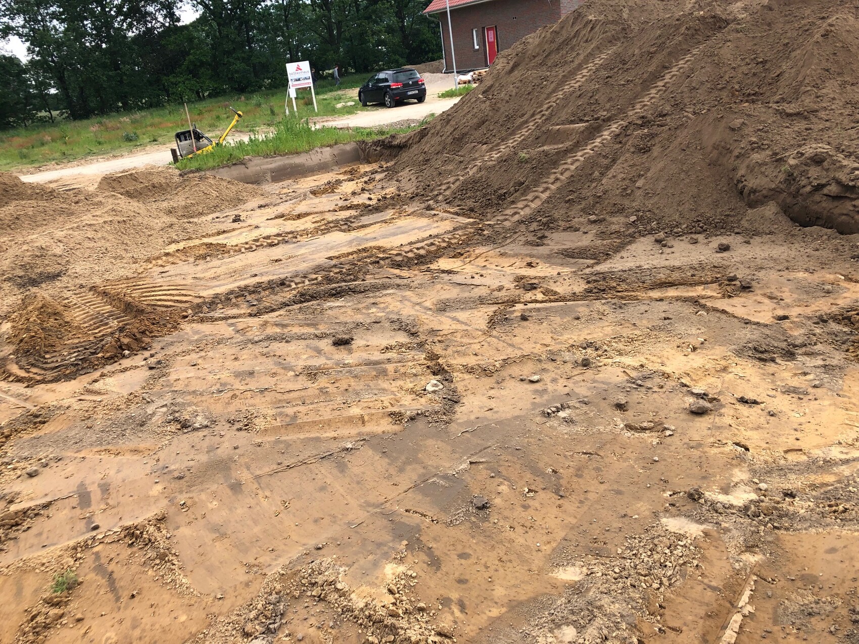 Construction site with large earth masses, traces of construction machinery in the mud, sand piles in the background.
