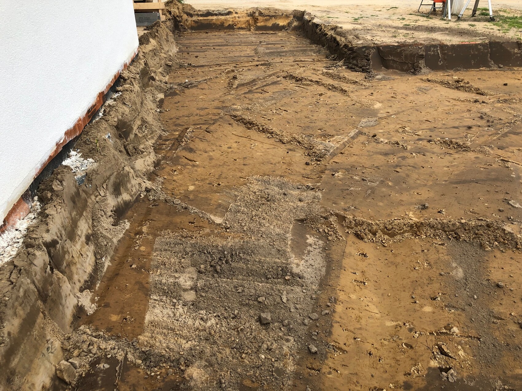 Construction site: trench next to the house wall, exposed foundation and visible soil.