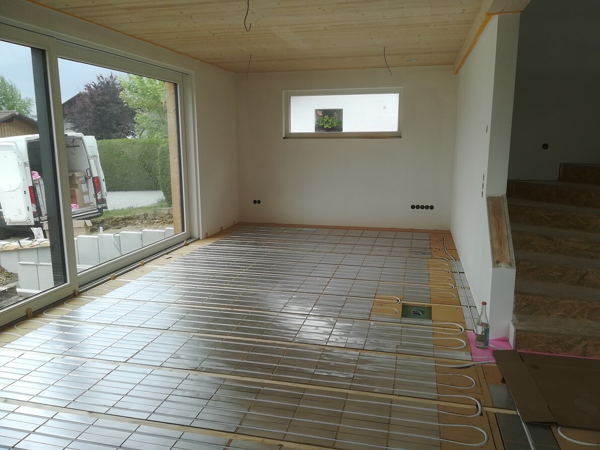 Modern construction room with laid underfloor heating pipes, glass facade, and staircase on the right.