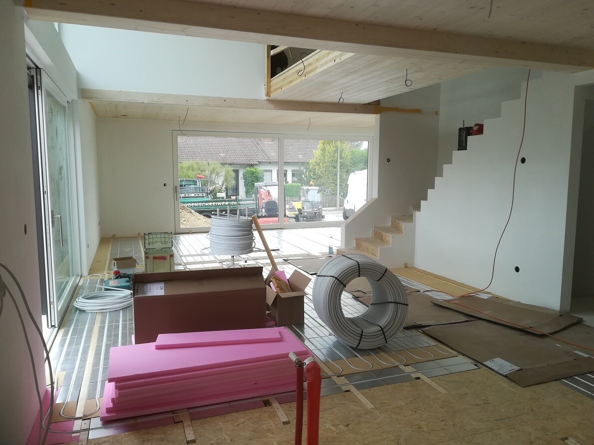 Interior of a construction site: shell construction, pink insulation boards, wire rolls, glass facade, open staircase.