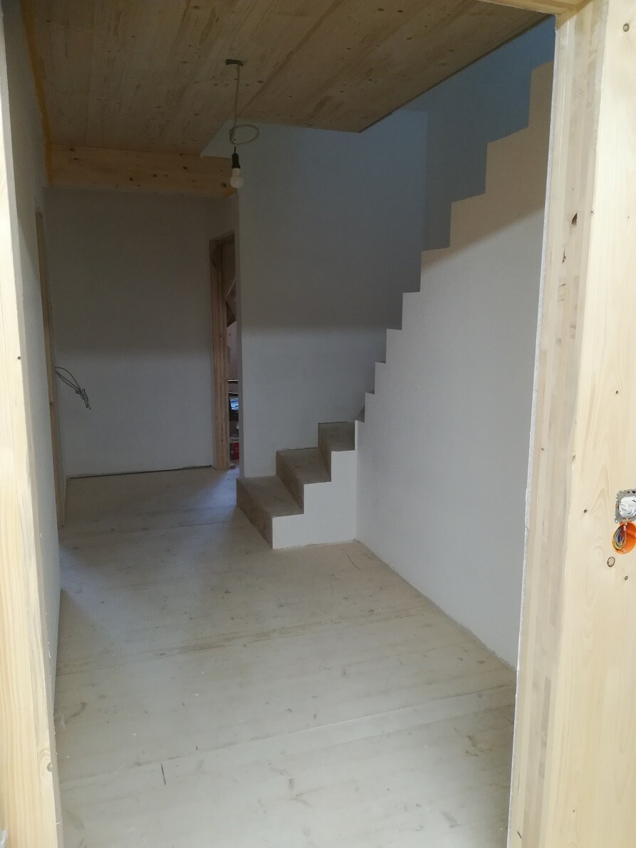 Shell construction: interior with gray wall, concrete stairs attached to the wall on the right, wooden ceiling.