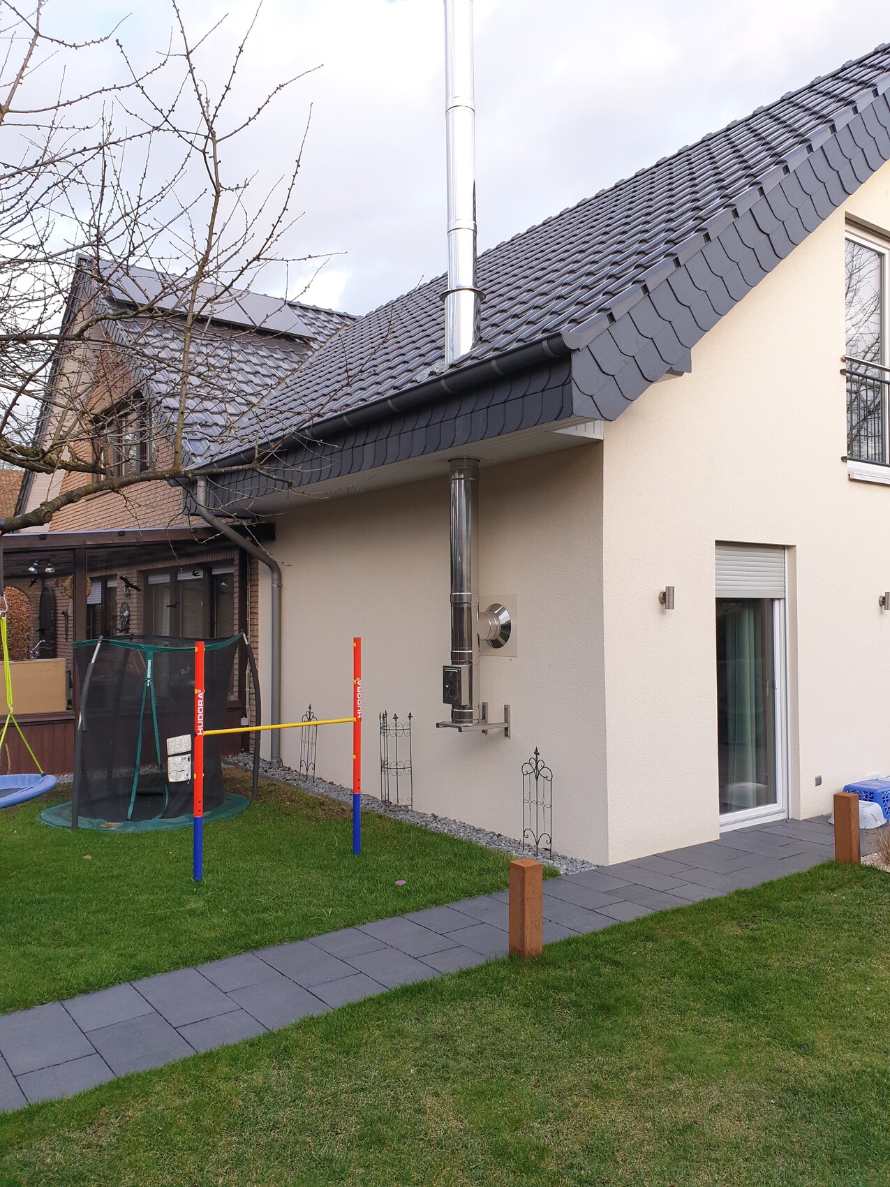 Modern detached house with stainless steel chimney on the roof; garden with trampoline.