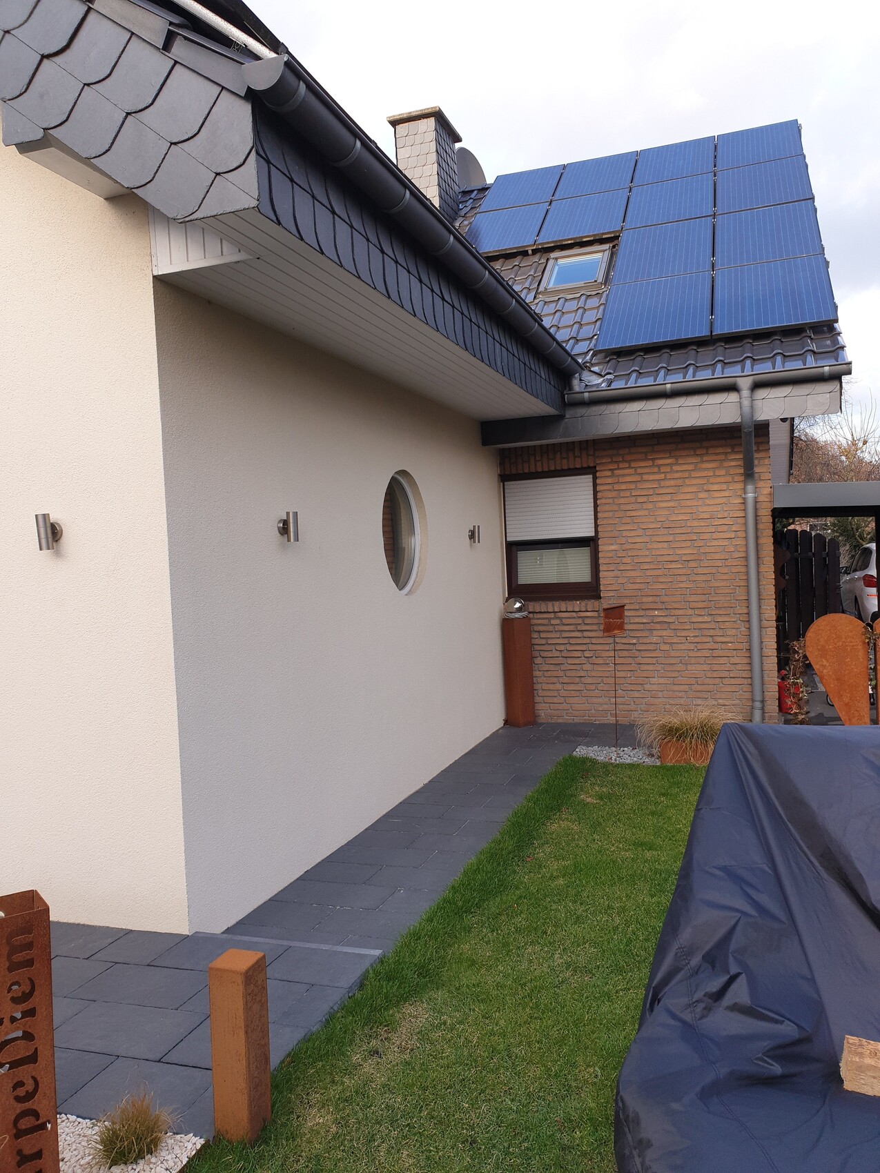 Exterior view of a house with blue solar panels on the roof, round window, and garden path.
