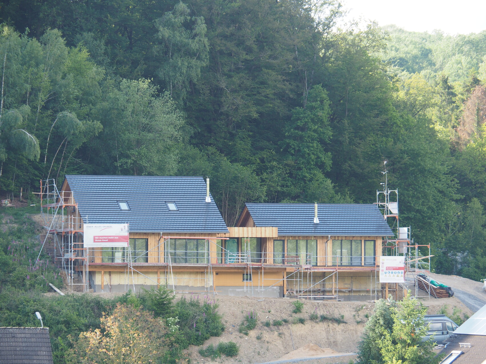 Two wooden houses under construction with scaffolding in front of a green forest background.