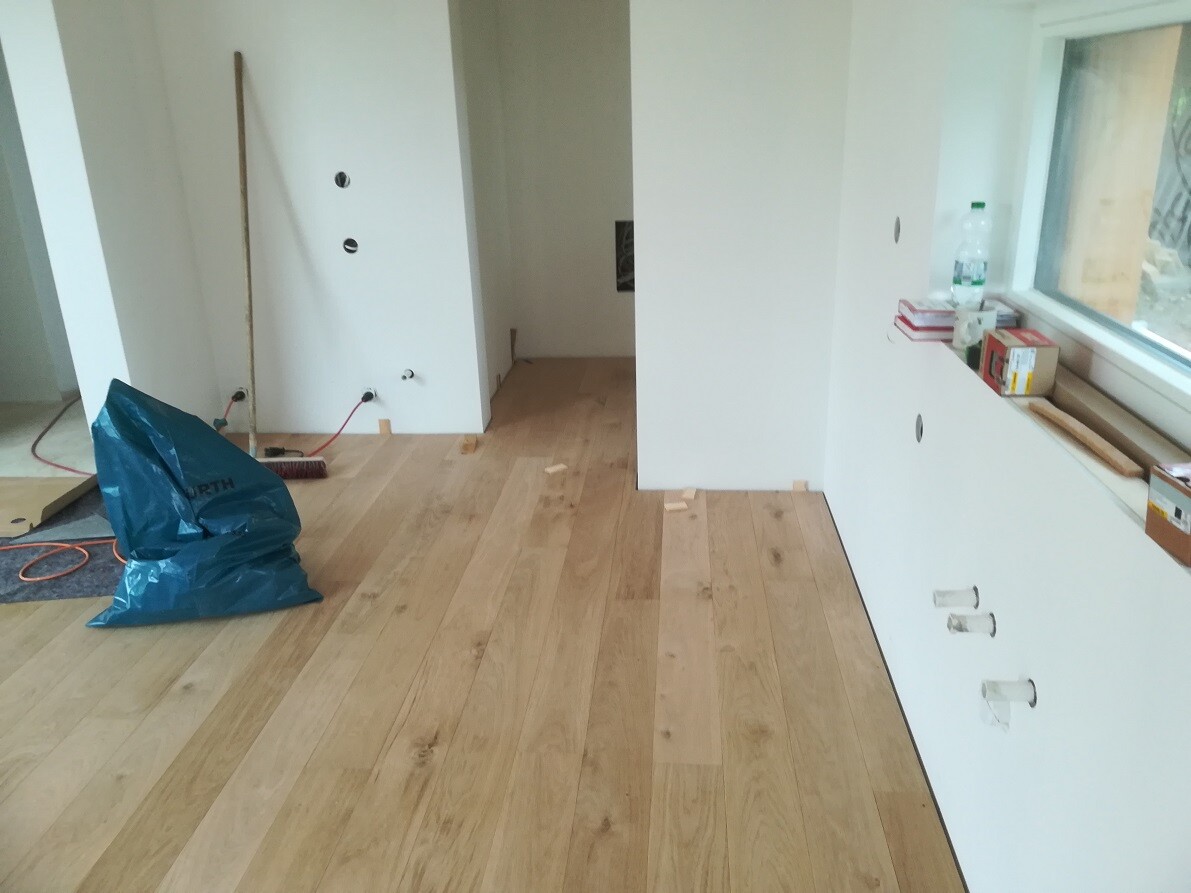 Room in renovation condition with wooden floor, plastering tools, blue garbage bag, and windowsill